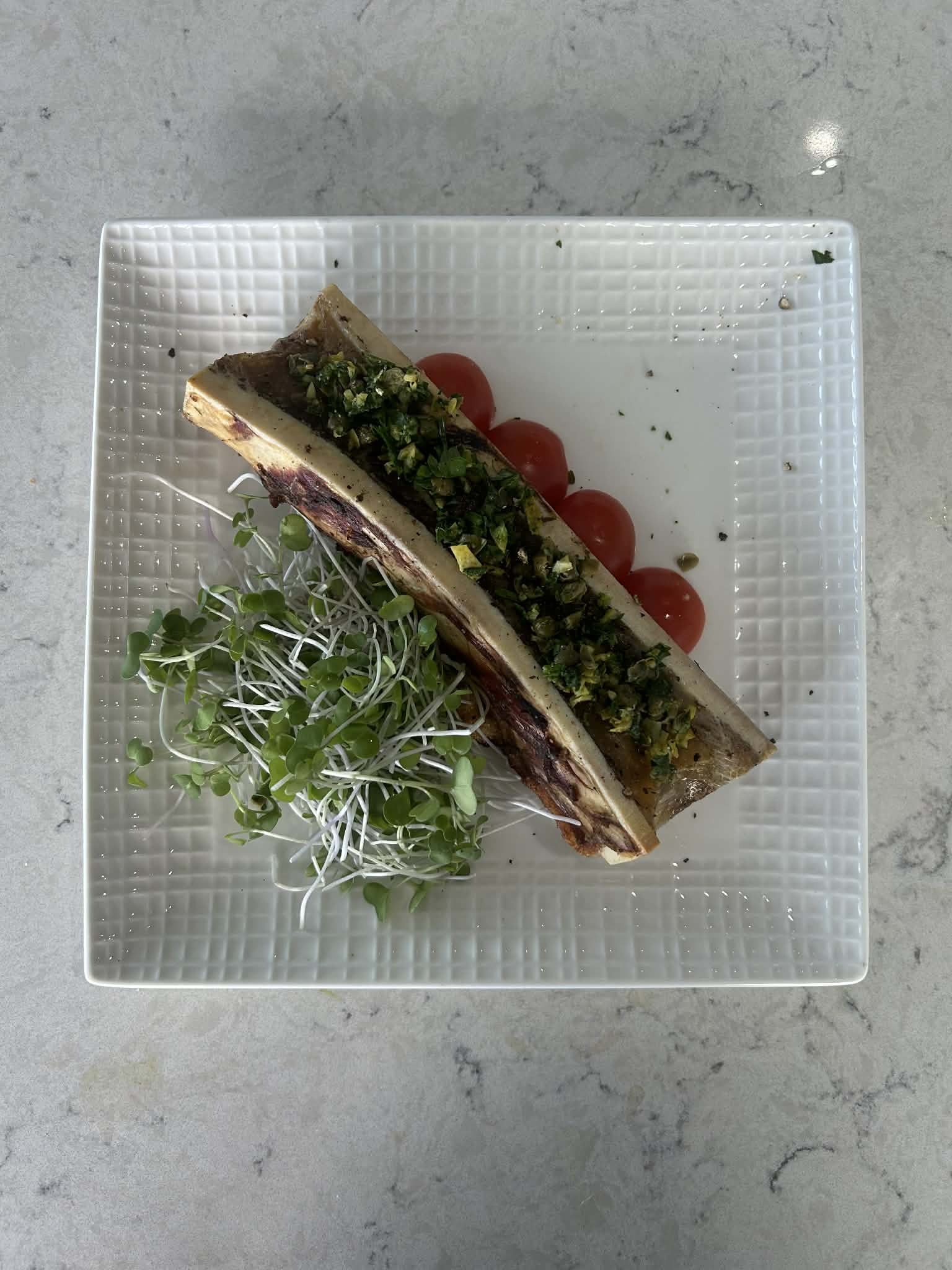 Roasted bone marrow plated with gremolata and cherry tomatoes